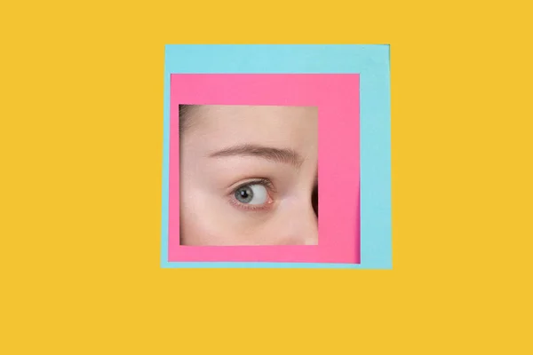 Face of caucasian woman peeking throught square in yellow background — Stock Photo, Image