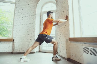 Koronavirüs salgını karantinası sırasında evde antrenman yapan genç beyaz adam spor yapıyor, aerobik yapıyor. İzolasyon sırasında sportif kalmak.