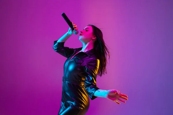 Potret penyanyi perempuan kaukasia terisolasi di latar belakang studio ungu dalam cahaya neon — Stok Foto