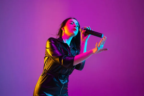 Blank vrouwelijke zangeres portret geïsoleerd op paars studio achtergrond in neon licht — Stockfoto
