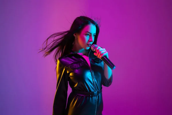 Портрет кавказской певицы, выделенный на фиолетовом фоне студии в неоновом свете — стоковое фото