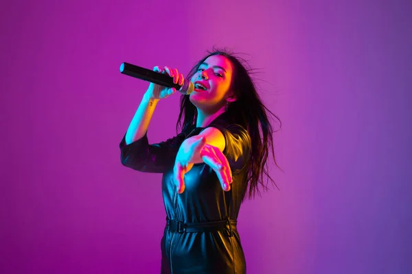 Biała kobieta piosenkarka portret izolowany na fioletowym tle studio w świetle neonu — Zdjęcie stockowe