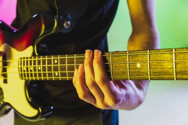 Müzisyen ellerini kapat. Gradyan stüdyo arka planında bas gitar çal.