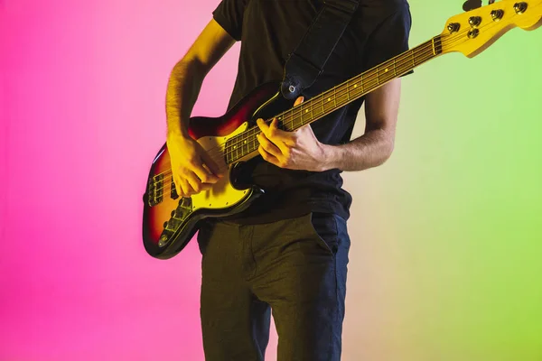 Young caucasian musician playing bass guitar in neon light on pink-green background — Stock Photo, Image