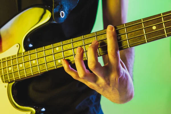 Close up musician hands playing bass guitar on gradient studio background in neon light