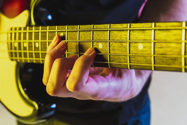 Fechar mãos músico tocando baixo no fundo do estúdio gradiente em luz de néon — Fotografia de Stock