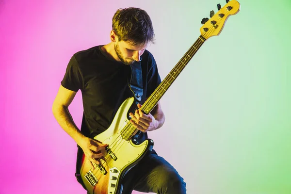 Joven músico caucásico tocando el bajo en luz de neón sobre fondo rosa-verde — Foto de Stock