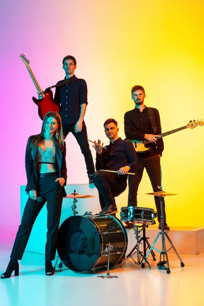 Jóvenes músicos caucásicos, banda actuando en luz de neón en el fondo del estudio gradiente — Foto de Stock