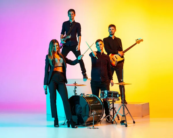 Jóvenes músicos caucásicos, banda actuando en luz de neón en el fondo del estudio gradiente —  Fotos de Stock