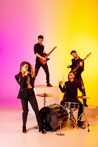 Young caucasian musicians, band performing in neon light on gradient studio background