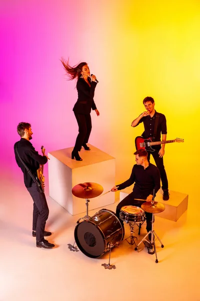 Young caucasian musicians, band performing in neon light on gradient studio background — Stock Photo, Image