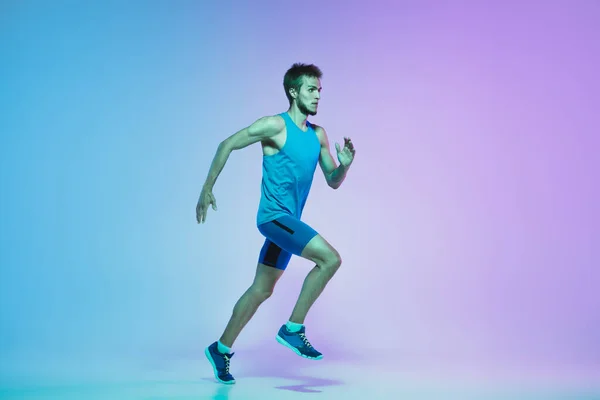 Retrato de comprimento total de ativo jovem caucasiano correndo, homem jogging no fundo do estúdio gradiente em luz de néon — Fotografia de Stock