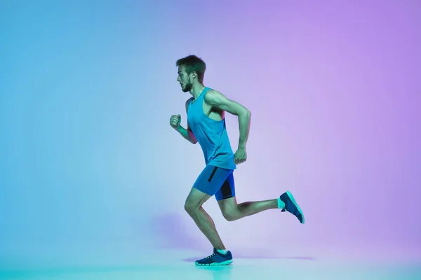 Retrato de comprimento total de ativo jovem caucasiano correndo, homem jogging no fundo do estúdio gradiente em luz de néon — Fotografia de Stock