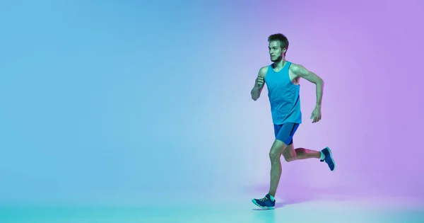 Full length portrait of active young caucasian running, jogging man op gradiënt studio achtergrond in neon licht — Stockfoto