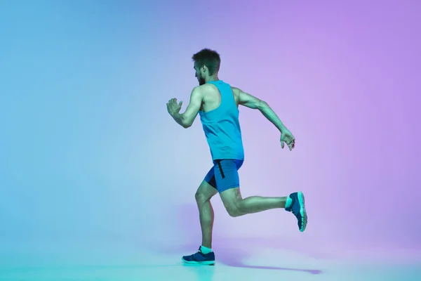 Ganztägiges Porträt eines aktiven jungen kaukasischen Lauf- und Joggingmannes auf Gradienten-Studiohintergrund im Neonlicht — Stockfoto