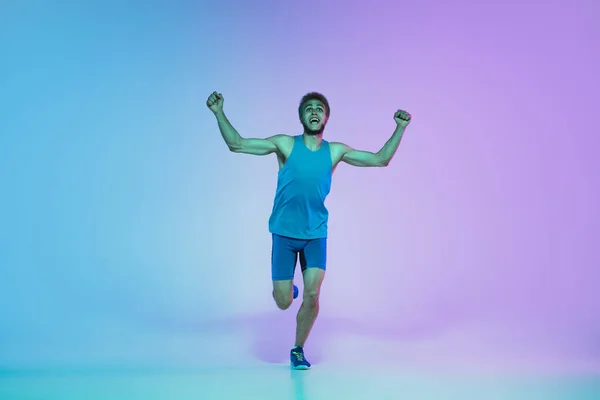 Full length portrait of active young caucasian running, jogging man on gradient studio background in neon light — Stock Photo, Image