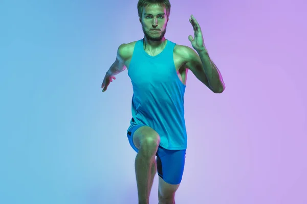 Full length portrait of active young caucasian running, jogging man op gradiënt studio achtergrond in neon licht — Stockfoto