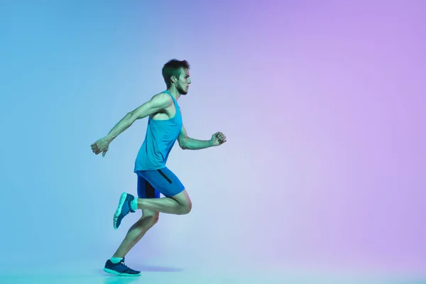 Full längd porträtt av aktiva unga kaukasiska kör, jogging man på lutning studio bakgrund i neon ljus — Stockfoto