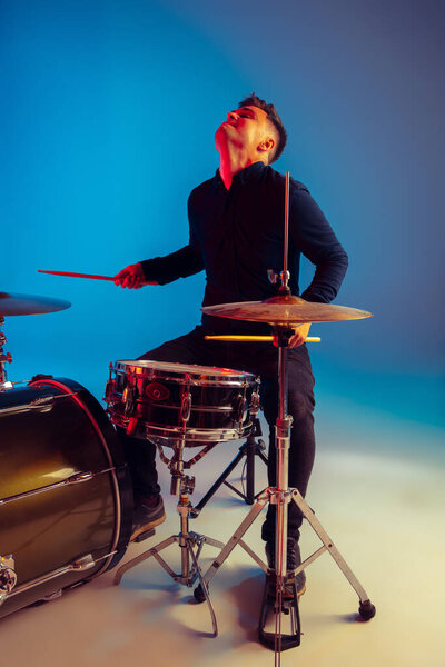 Caucasian male drummer improvising isolated on blue studio background in neon light