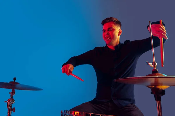Kaukasischer Schlagzeuger improvisiert isoliert auf blauem Studiohintergrund in Neonlicht — Stockfoto