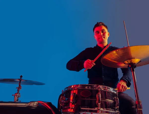 Caucasiano baterista masculino improvisando isolado em fundo estúdio azul em luz de néon — Fotografia de Stock