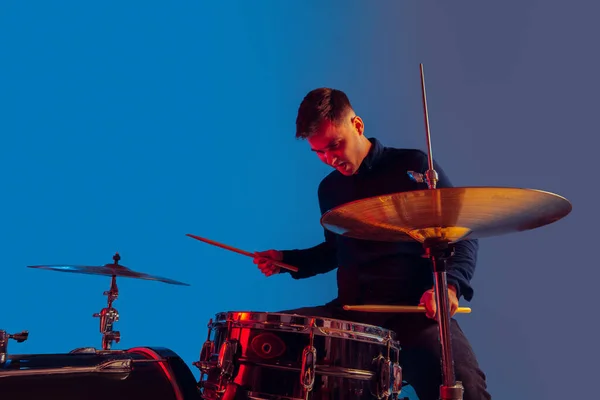 Caucasiano baterista masculino improvisando isolado em fundo estúdio azul em luz de néon — Fotografia de Stock