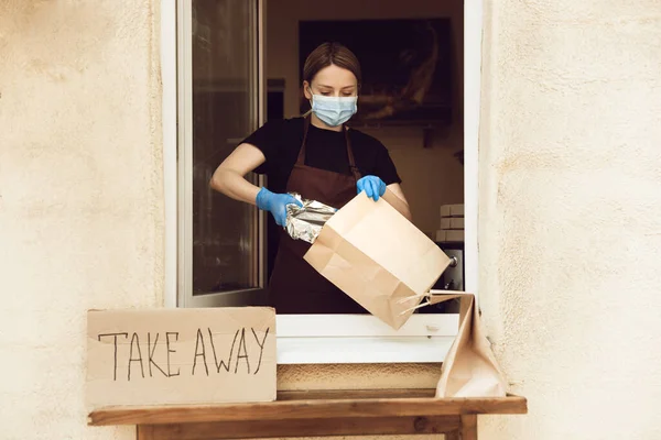 Frau bereitet Getränke und Mahlzeiten zu, trägt Mundschutz und Handschuhe. Kontaktloser Lieferservice während der Coronavirus-Pandemie unter Quarantäne. Nur Konzept mitnehmen. — Stockfoto