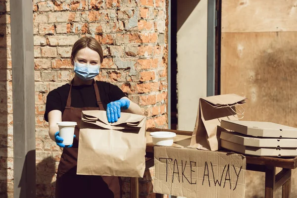 Frau bereitet Getränke und Mahlzeiten zu, trägt Mundschutz und Handschuhe. Kontaktloser Lieferservice während der Coronavirus-Pandemie unter Quarantäne. Nur Konzept mitnehmen. — Stockfoto