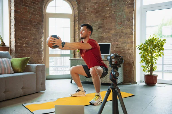 Jonge blanke man training thuis tijdens quarantaine van coronavirus uitbraak, het doen van oefeningen van fitness, aërobe. Sportief blijven tijdens isolatie. — Stockfoto