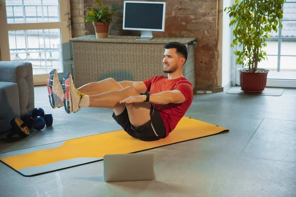 Jonge blanke man training thuis tijdens quarantaine van coronavirus uitbraak, het doen van oefeningen van fitness, aërobe. Sportief blijven tijdens isolatie. — Stockfoto