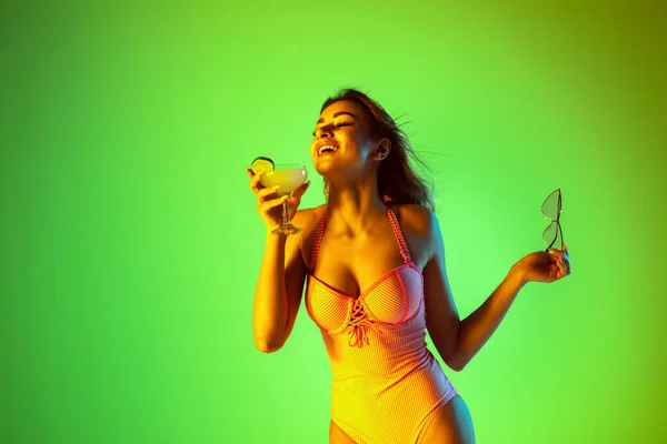 Hermosa chica en traje de baño de moda aislado en el fondo del estudio gradiente en luz de neón. Verano, resort, moda y concepto de fin de semana —  Fotos de Stock