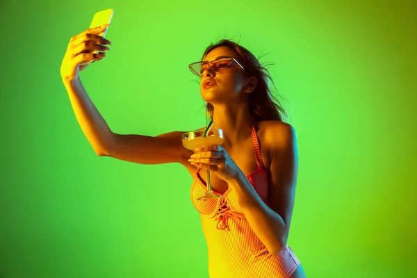 Menina bonita em maiô elegante isolado no fundo do estúdio gradiente em luz de néon. Verão, resort, moda e conceito de fim de semana — Fotografia de Stock