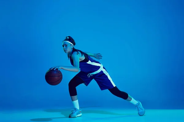 Joven jugador de baloncesto femenino caucásico aislado en fondo estudio azul en luz de neón —  Fotos de Stock
