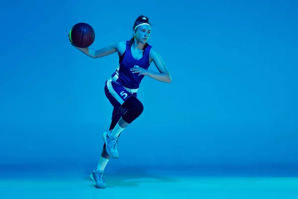 Giovane giocatore di basket femminile caucasico isolato su sfondo blu studio in luce al neon — Foto Stock
