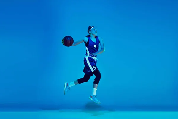 Beyaz tenli genç bayan basketbolcu mavi stüdyo arka planında neon ışıkta izole edilmiş. — Stok fotoğraf