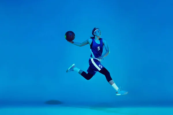 Jovem caucasiano jogador de basquete feminino isolado no fundo do estúdio azul em luz de néon — Fotografia de Stock