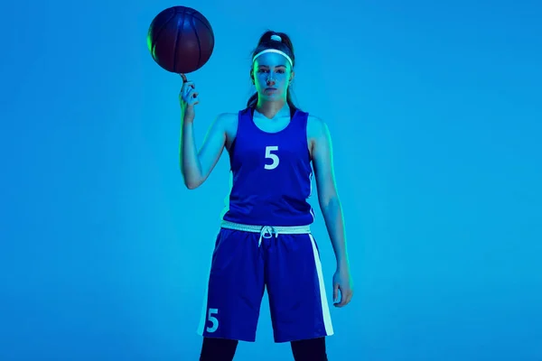 Jovem caucasiano jogador de basquete feminino isolado no fundo do estúdio azul em luz de néon — Fotografia de Stock