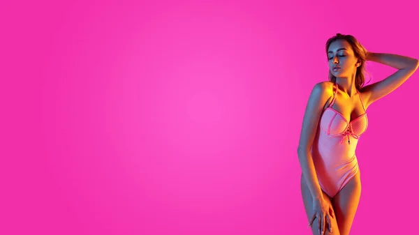 Mooi meisje in modieuze badpak geïsoleerd op gradiënt studio achtergrond in neon licht. Zomer, resort, mode en weekend concept — Stockfoto