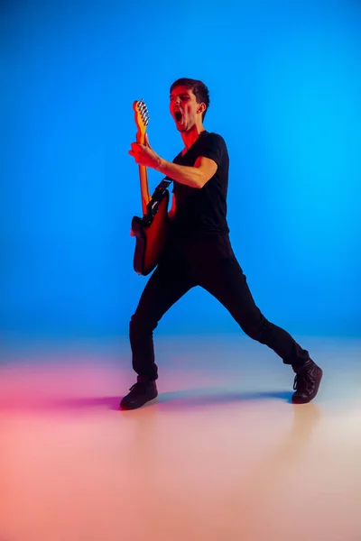 젊은 코카서스 음악가가 푸른 배경에 네온등으로 기타를 연주하는 모습, 영감을 받은 모습 — 스톡 사진
