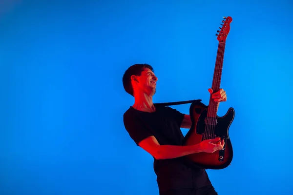 Fiatal kaukázusi zenész gitározik neon fény kék háttér, ihlette — Stock Fotó