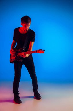 Genç beyaz müzisyen mavi arka planda neon ışıkta gitar çalıyor.