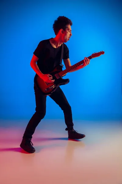 Junge kaukasische Musiker spielen Gitarre in Neonlicht auf blauem Hintergrund, inspiriert — Stockfoto