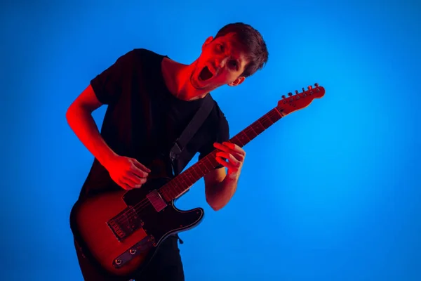 Fiatal kaukázusi zenész gitározik neon fény kék háttér, ihlette — Stock Fotó