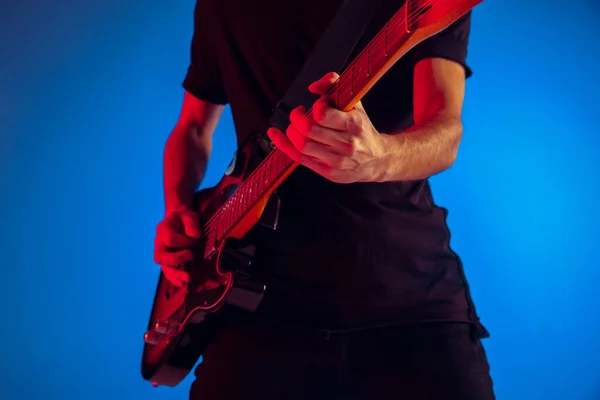 Jovem músico caucasiano tocando guitarra em luz de néon em fundo azul, inspirado — Fotografia de Stock