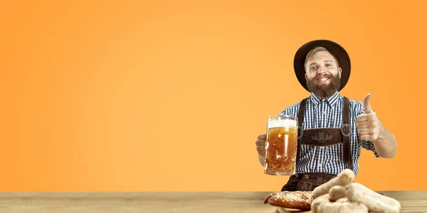 Посмішка чоловіка з пивом, одягненого в традиційний австрійський або баварський костюм, який тримає кухоль пива в пабі або студії. Святкування, Октоберфест, свято — стокове фото