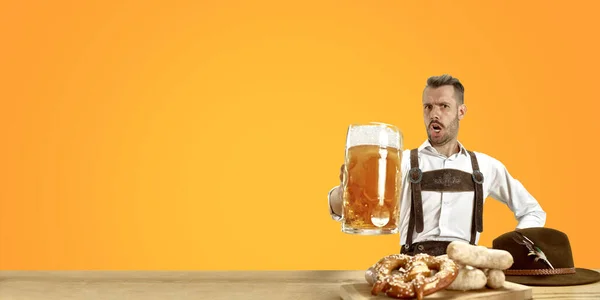 Homme souriant avec de la bière vêtue d'un costume traditionnel autrichien ou bavarois tenant une tasse de bière dans un pub ou un studio. La fête, l'oktoberfest, le festival — Photo