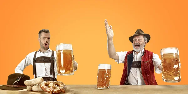 Hombres sonrientes con cerveza vestidos con el traje tradicional austriaco o bávaro sosteniendo taza de cerveza en un pub o estudio. La celebración, oktoberfest, festival —  Fotos de Stock