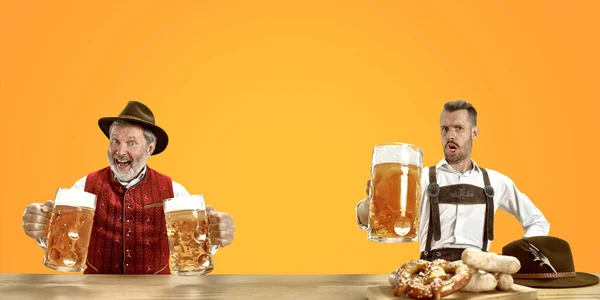 Hombres sonrientes con cerveza vestidos con el traje tradicional austriaco o bávaro sosteniendo taza de cerveza en un pub o estudio. La celebración, oktoberfest, festival —  Fotos de Stock