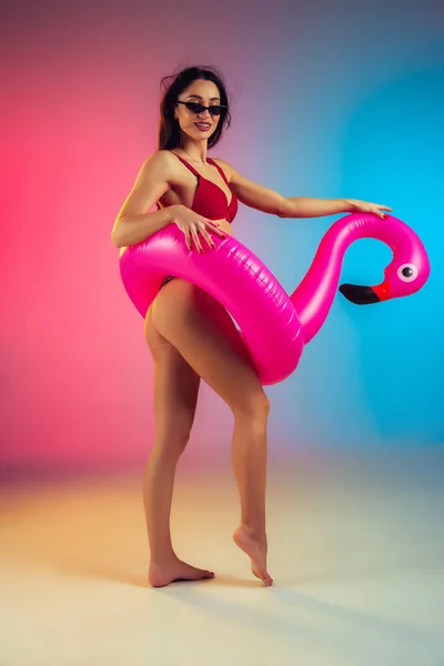 Retrato de moda de mujer joven en forma y deportiva con flamenco de goma en elegante traje de baño rojo sobre fondo degradado. Cuerpo perfecto listo para el verano . — Foto de Stock