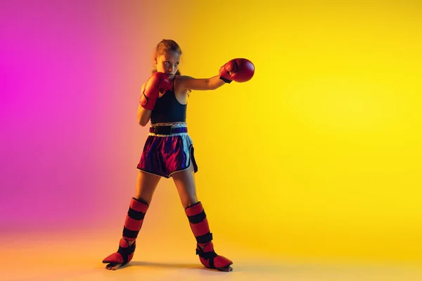 Petit caucasien entraînement kick boxer féminin sur fond dégradé en néon léger, actif et expressif — Photo